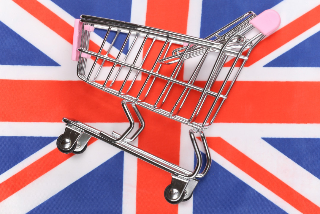 Mini supermarket trolley on blurred Great Britain flag background. Shopping concept.